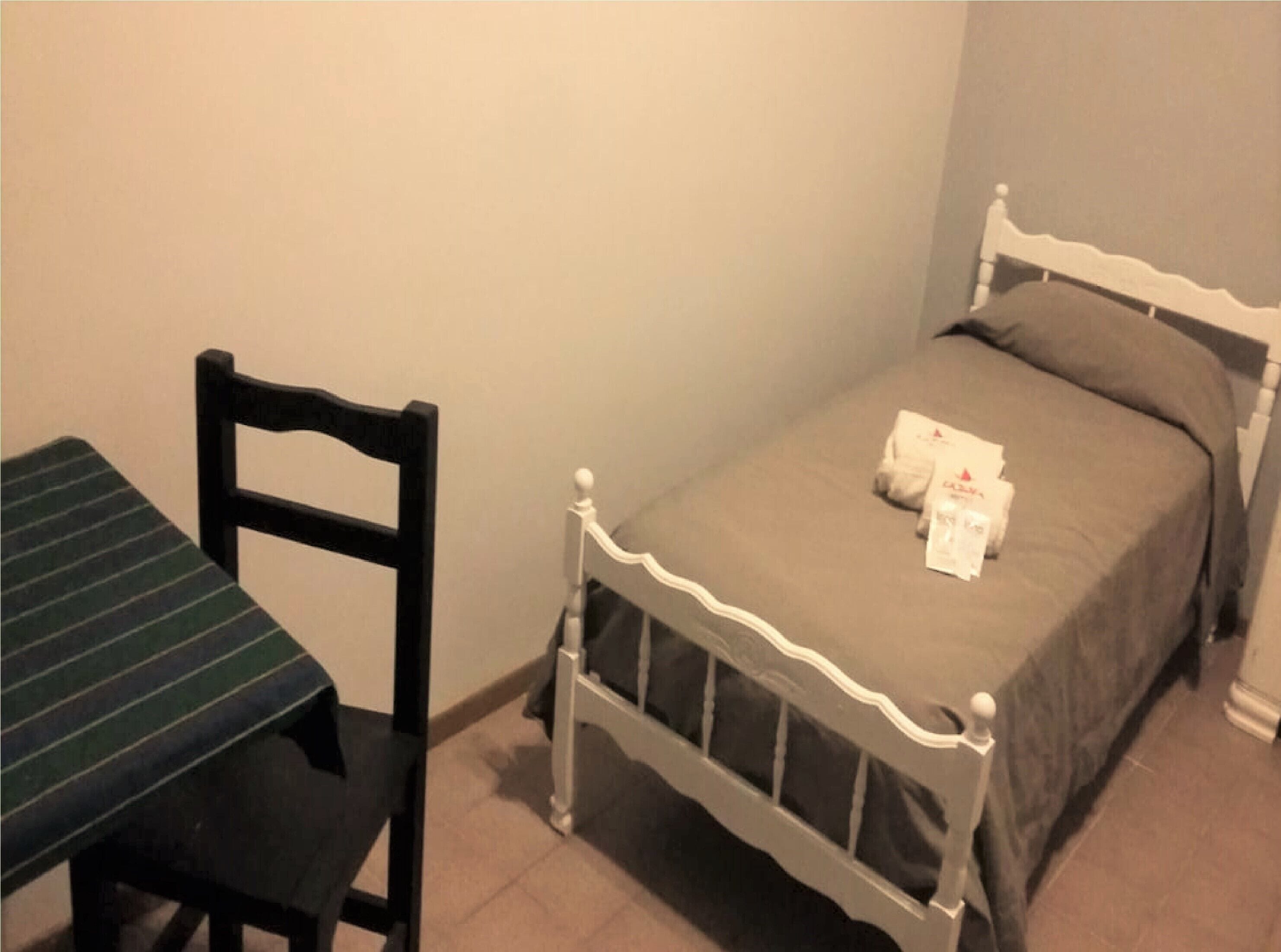 Een kleine kamer met een enkel bed, een stoel en een tafel.