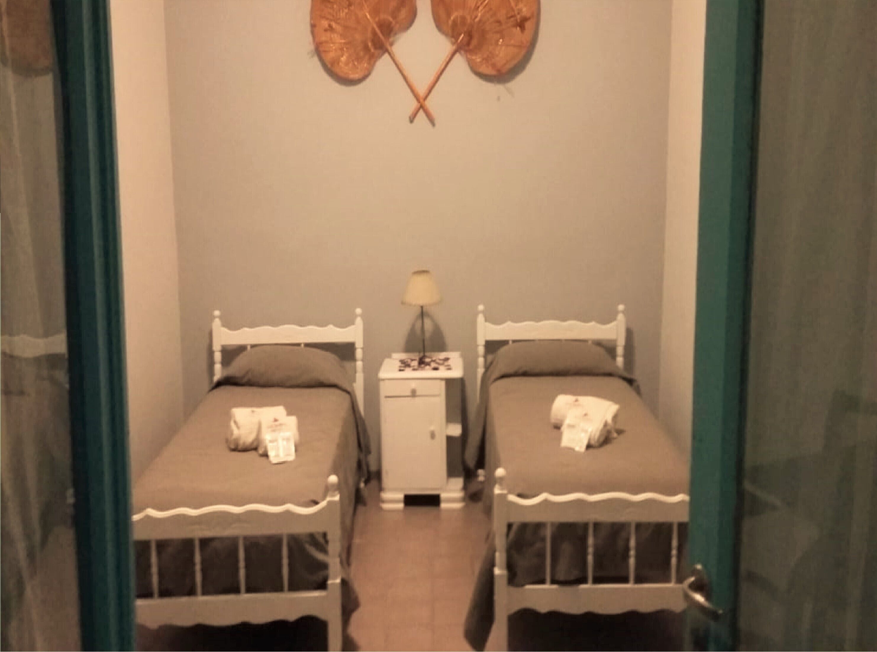 A small, dimly lit room with two single beds, a nightstand with a lamp, and a wall decoration.