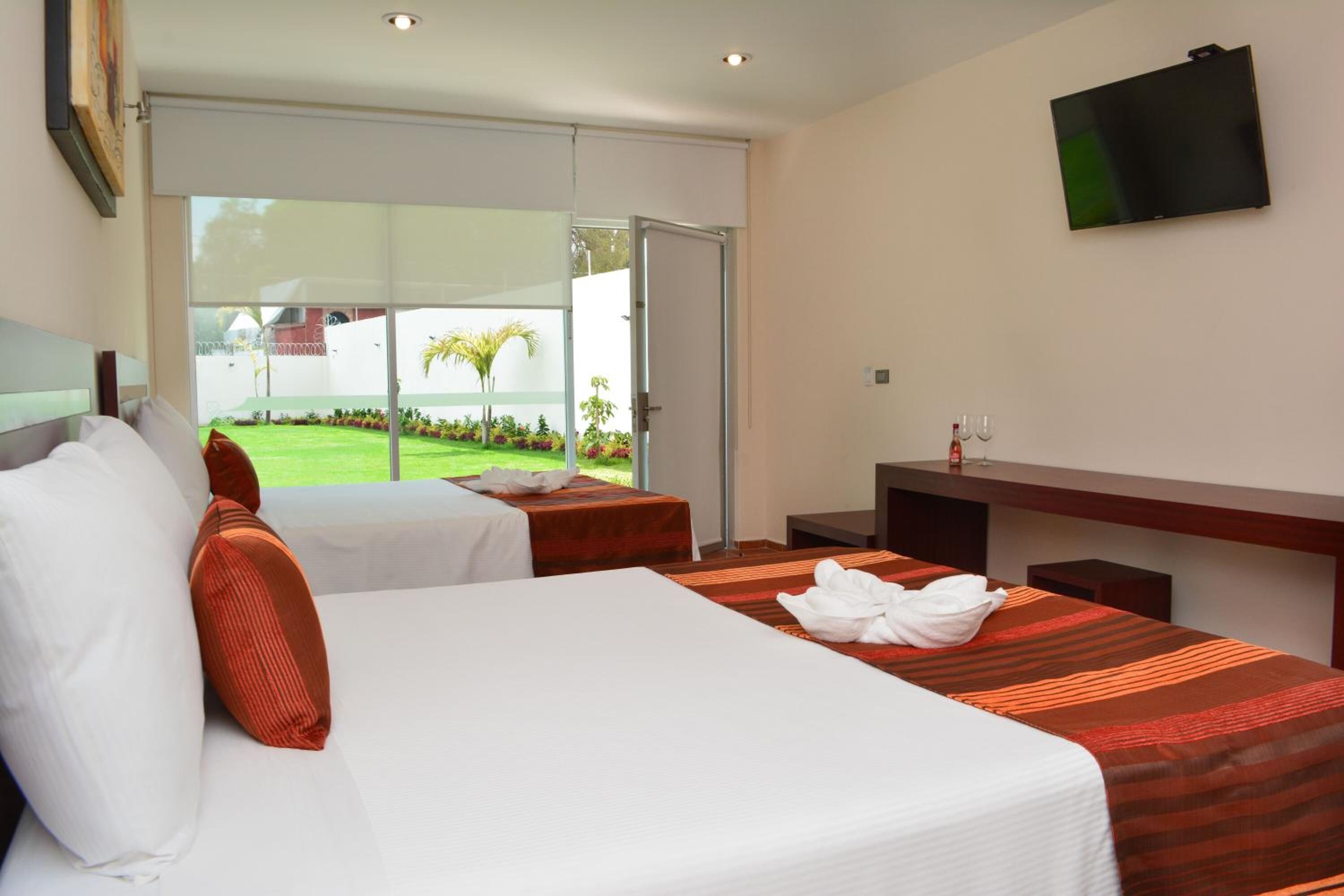 A hotel room with two beds, a TV mounted on the wall, and a sliding glass door leading to a garden.