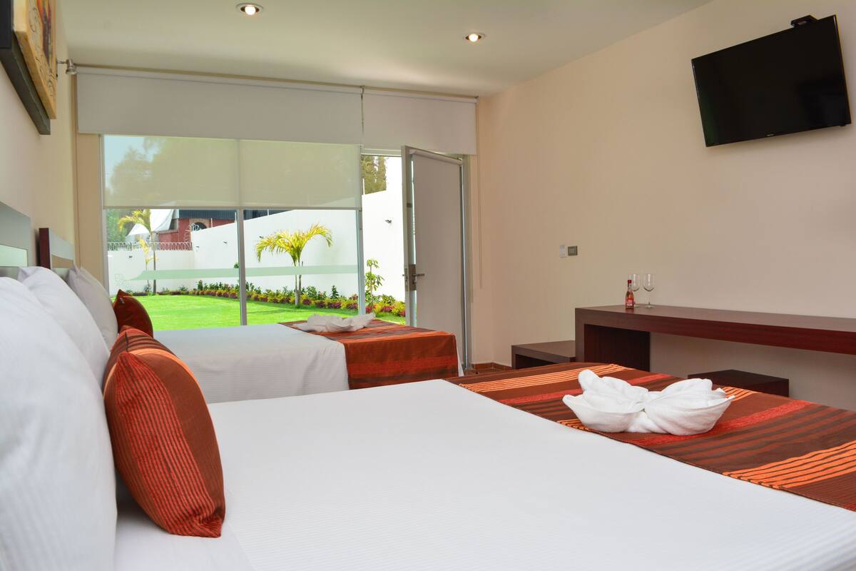 A hotel room with two beds, a TV, and a view of a garden.