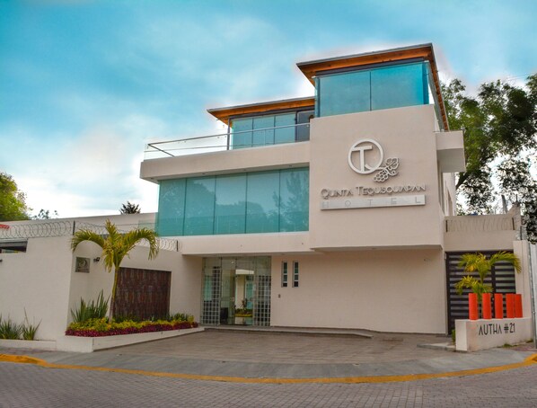 A modern hotel building with a large glass facade, a prominent logo, and a name sign.