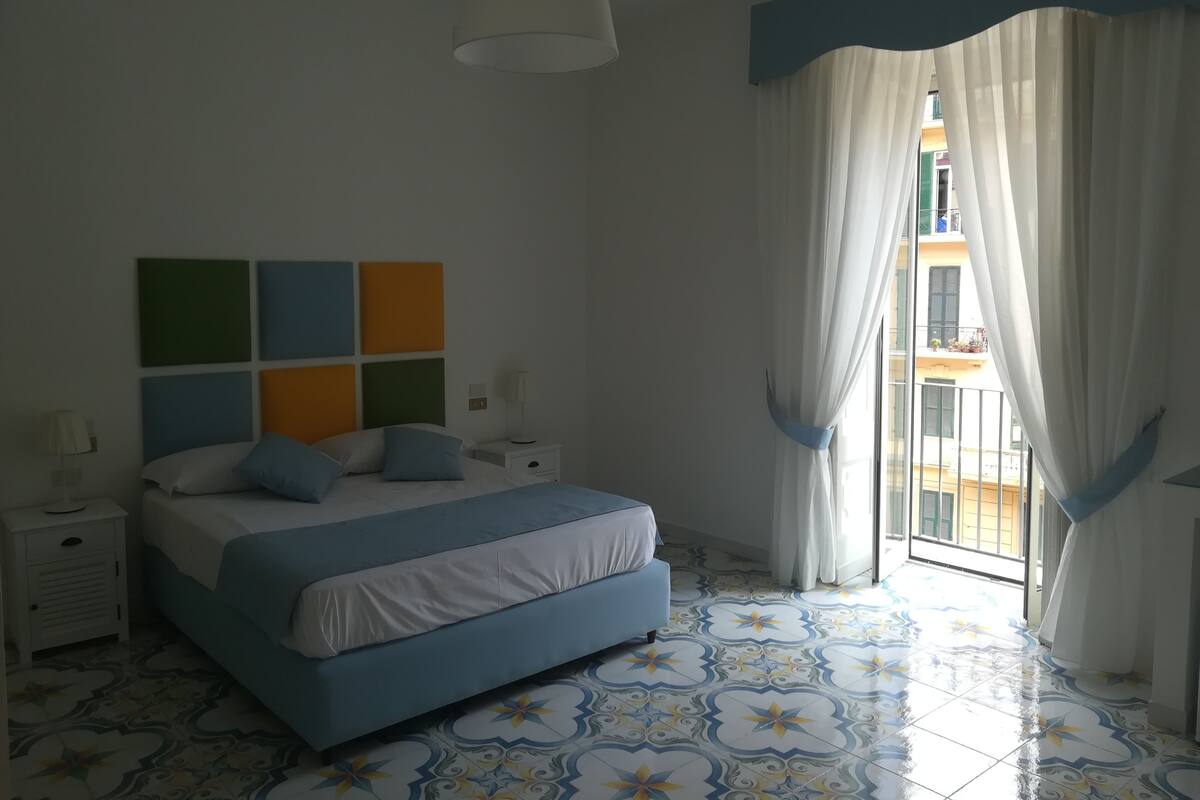 A bedroom with a bed, nightstands, a wall clock, and a window with curtains.