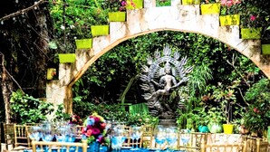 An outdoor dining area with a blue tablecloth, wooden chairs, and a statue under an archway. - Xolumado Inspiration Village by Karisma (Playa del Carmen)