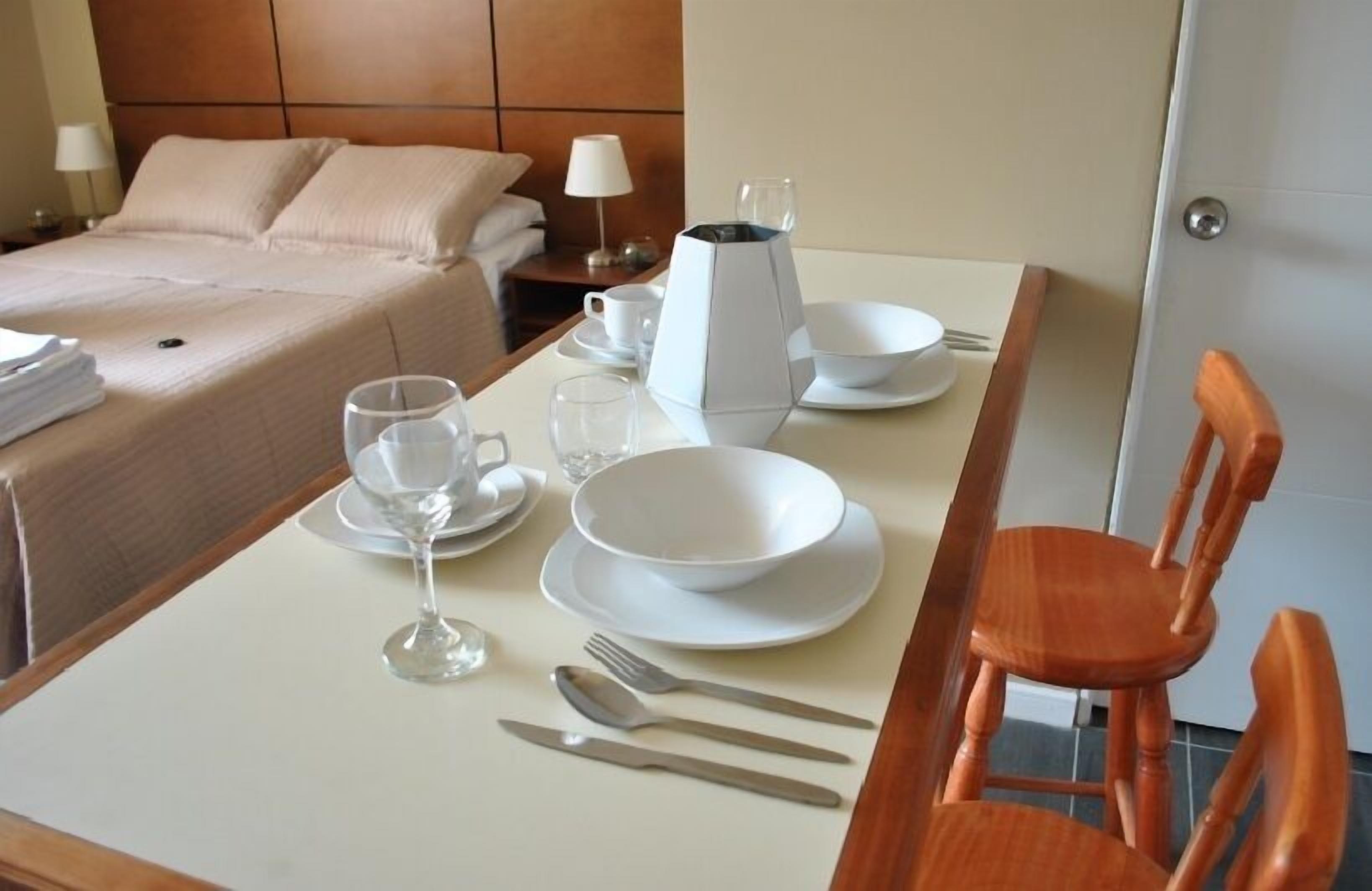 Une table de salle à manger bien dressée, avec des assiettes, des verres, des couverts et une cafetière, dans une chambre d’hôtel.