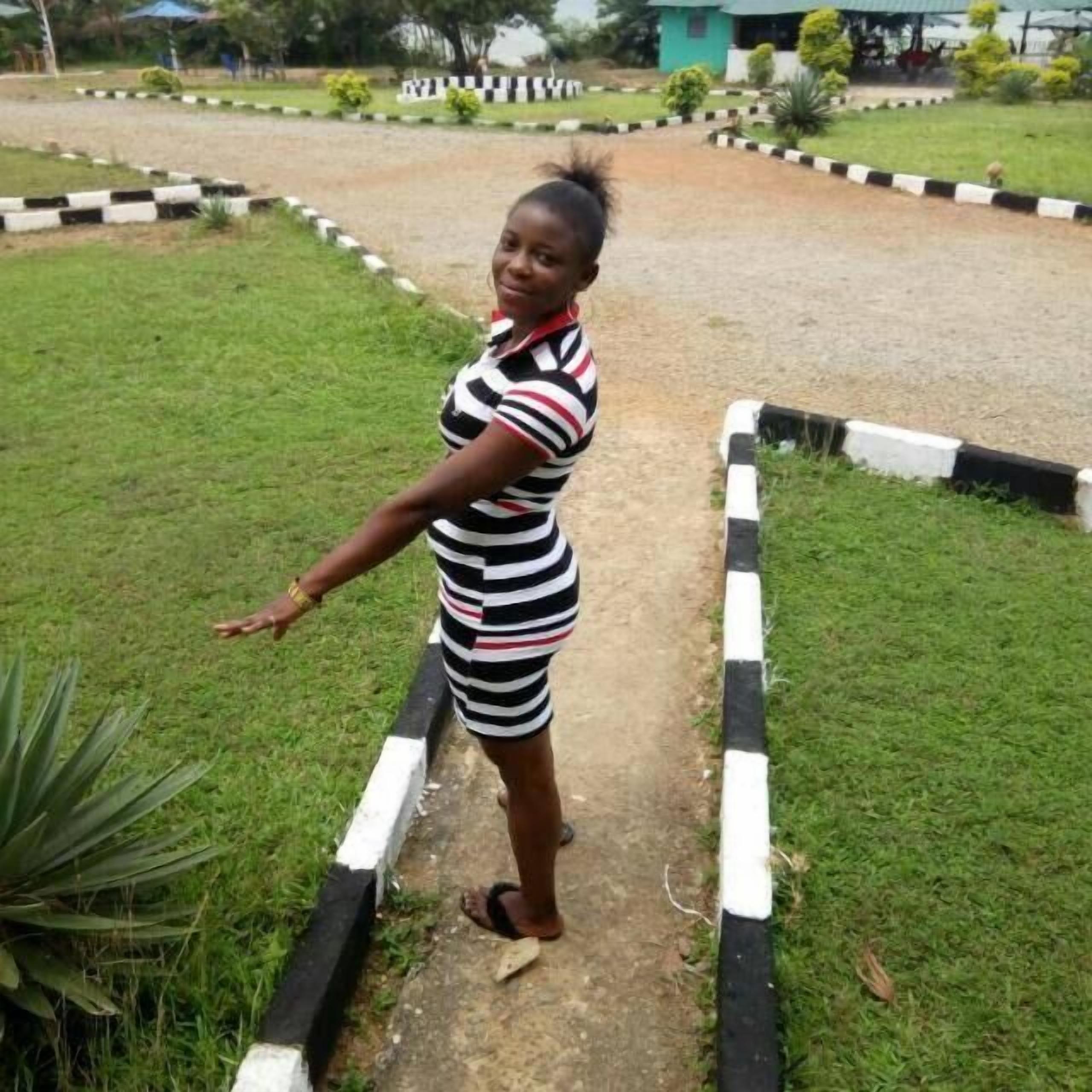 A person standing on a pathway with grass on either side, bordered by black and white curbs.