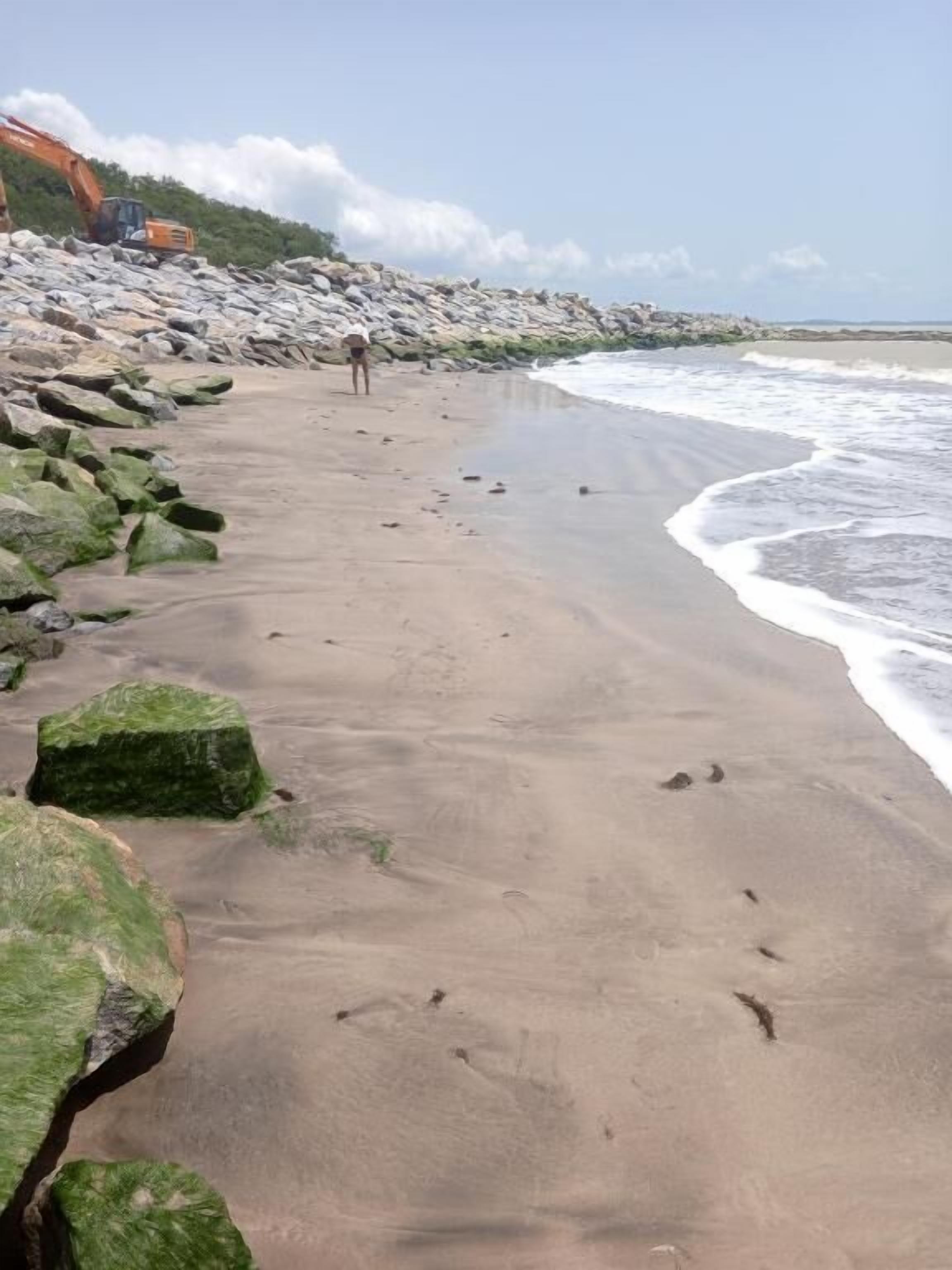 A beach with a rocky shoreline and a person walking.