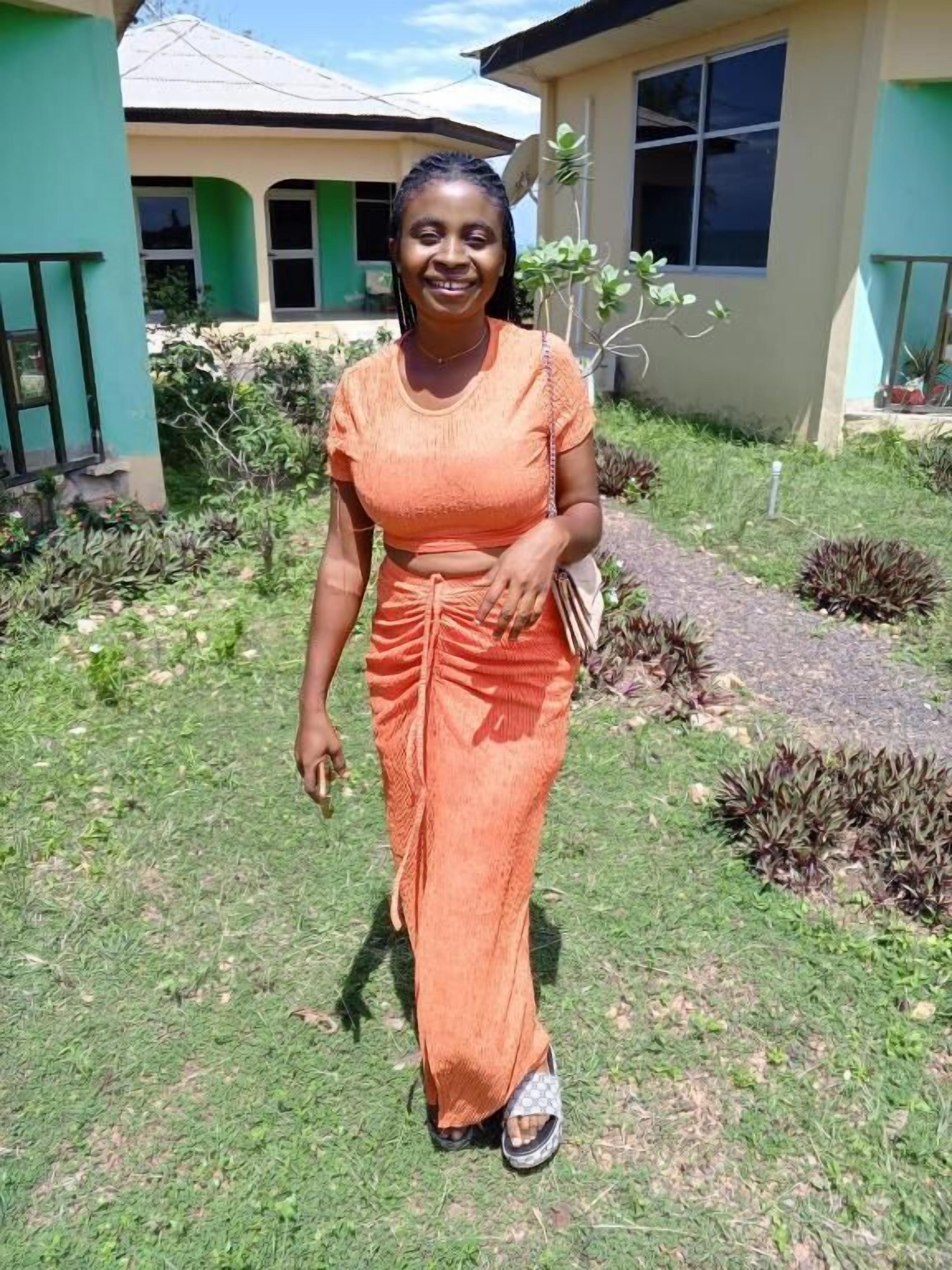 A person standing in a garden area with a house in the background.