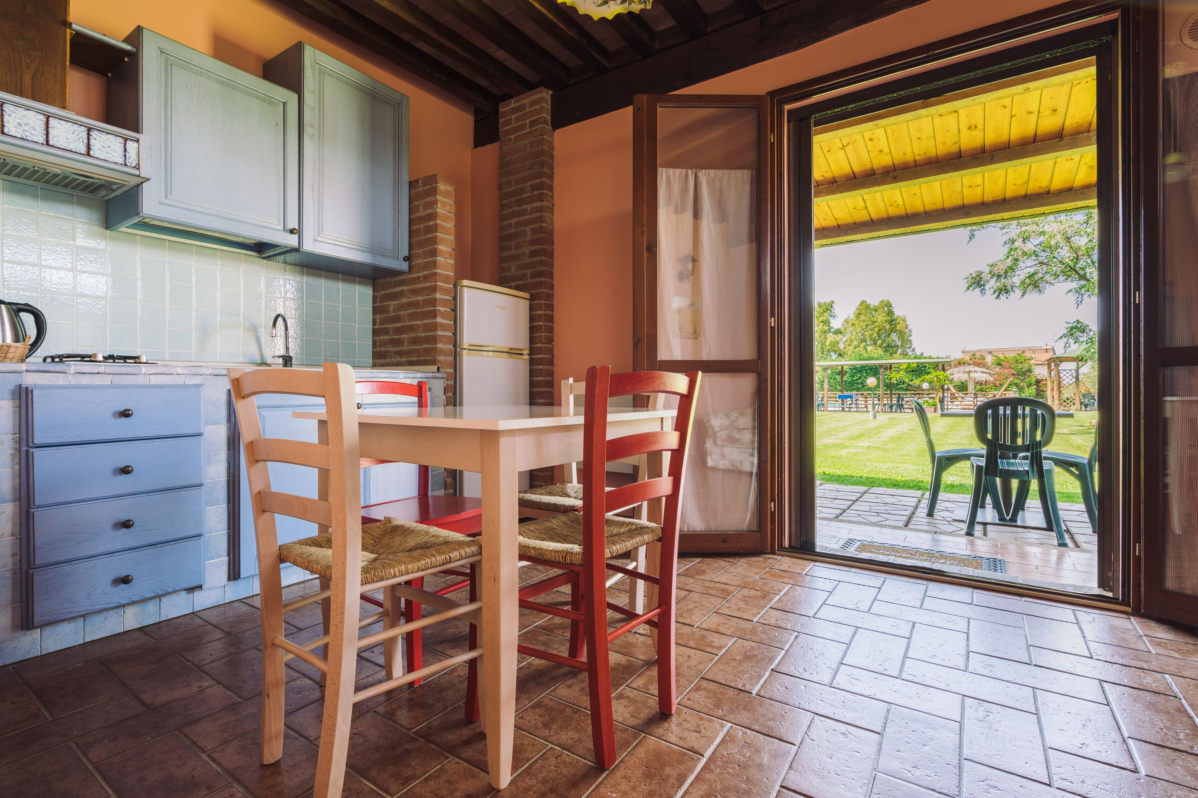 A kitchen with a dining area, a view of the garden through a glass door, and a brick wall.