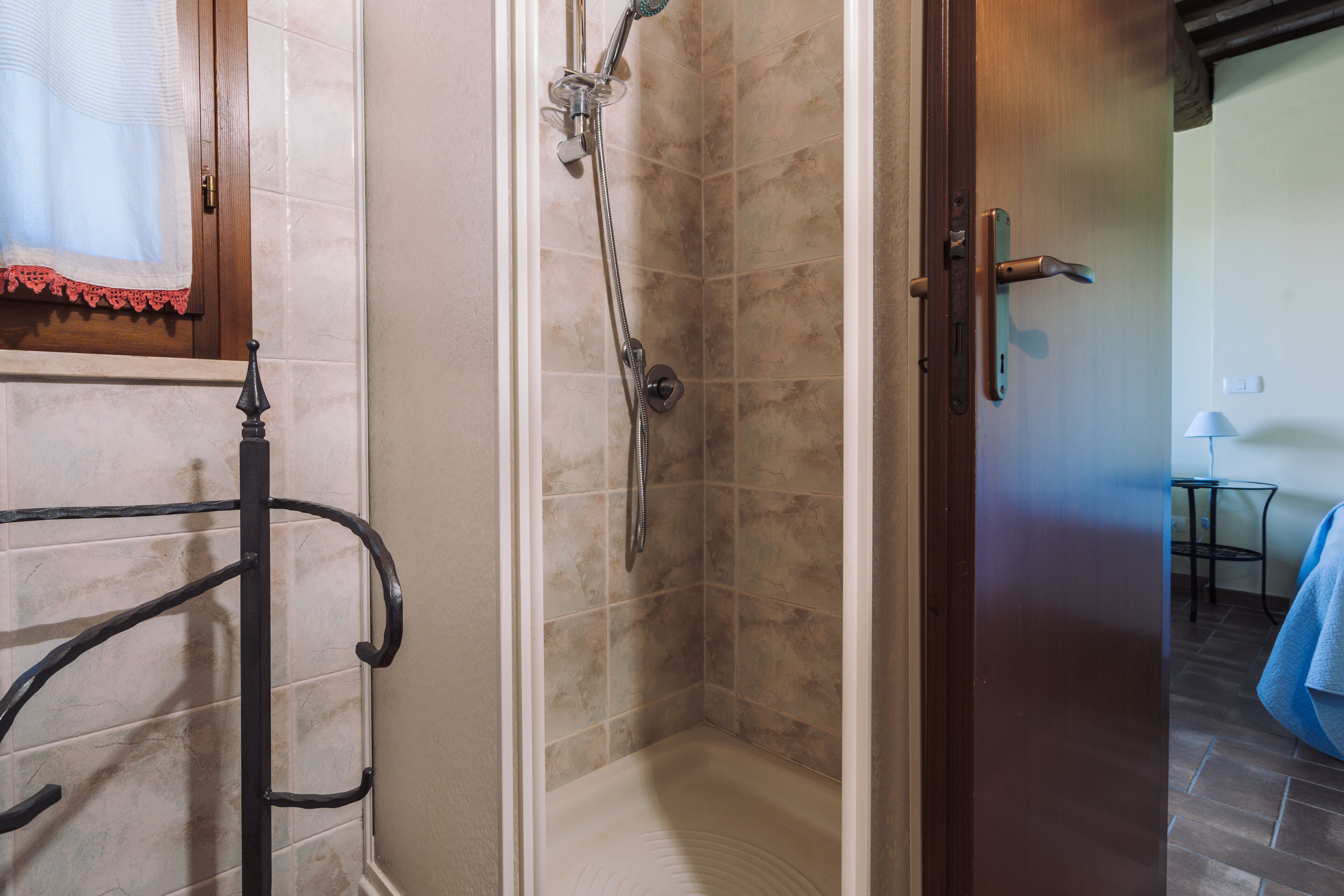 A bathroom with a shower, a towel rack, and a door leading to another room.