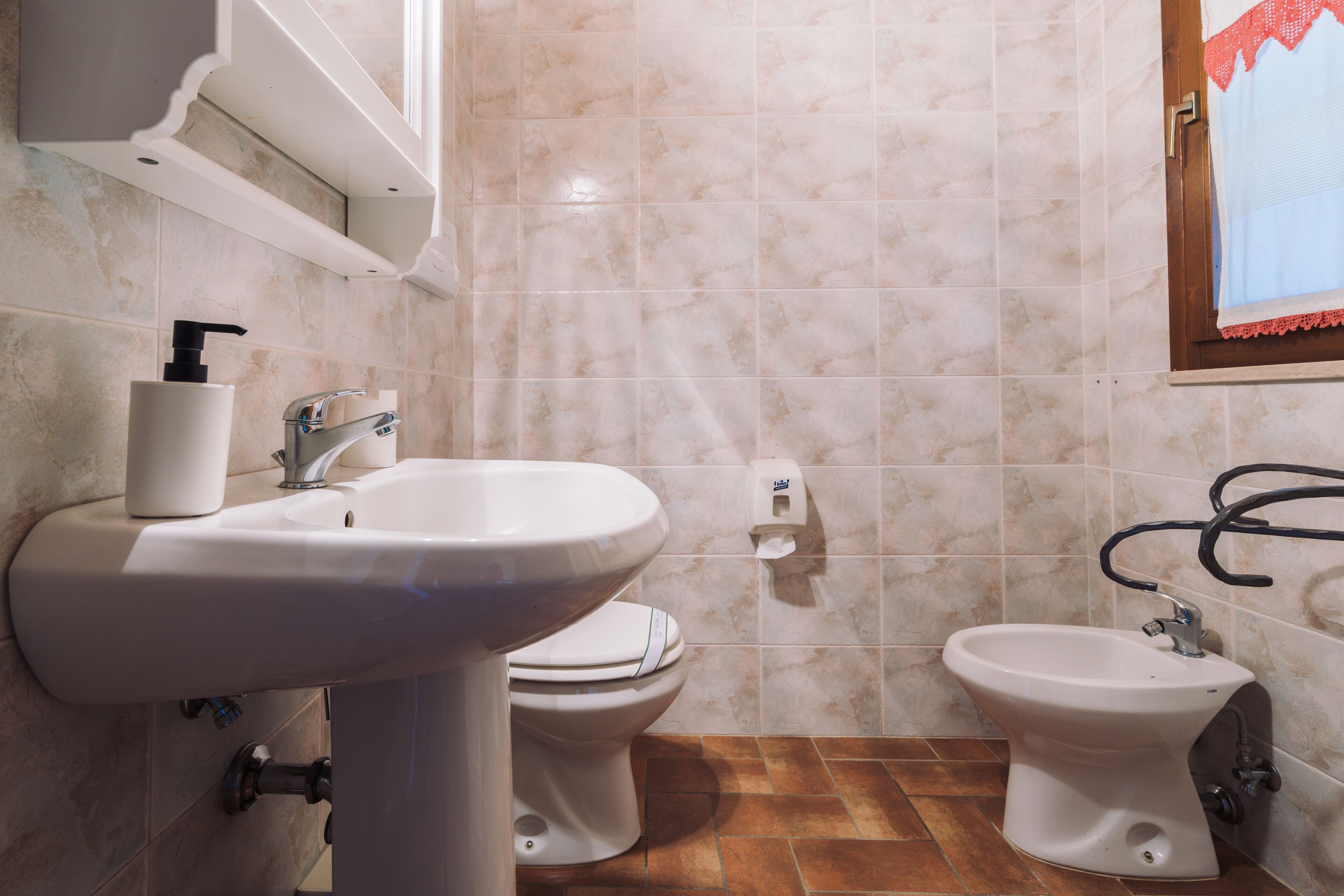 A bathroom with a sink, toilet, bidet, and a towel rack.