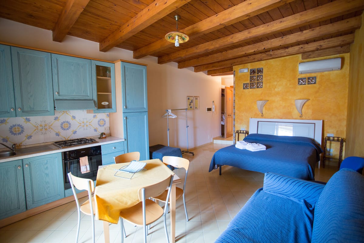 A room with a kitchen, a dining area, and a bedroom with a bed and a sofa.