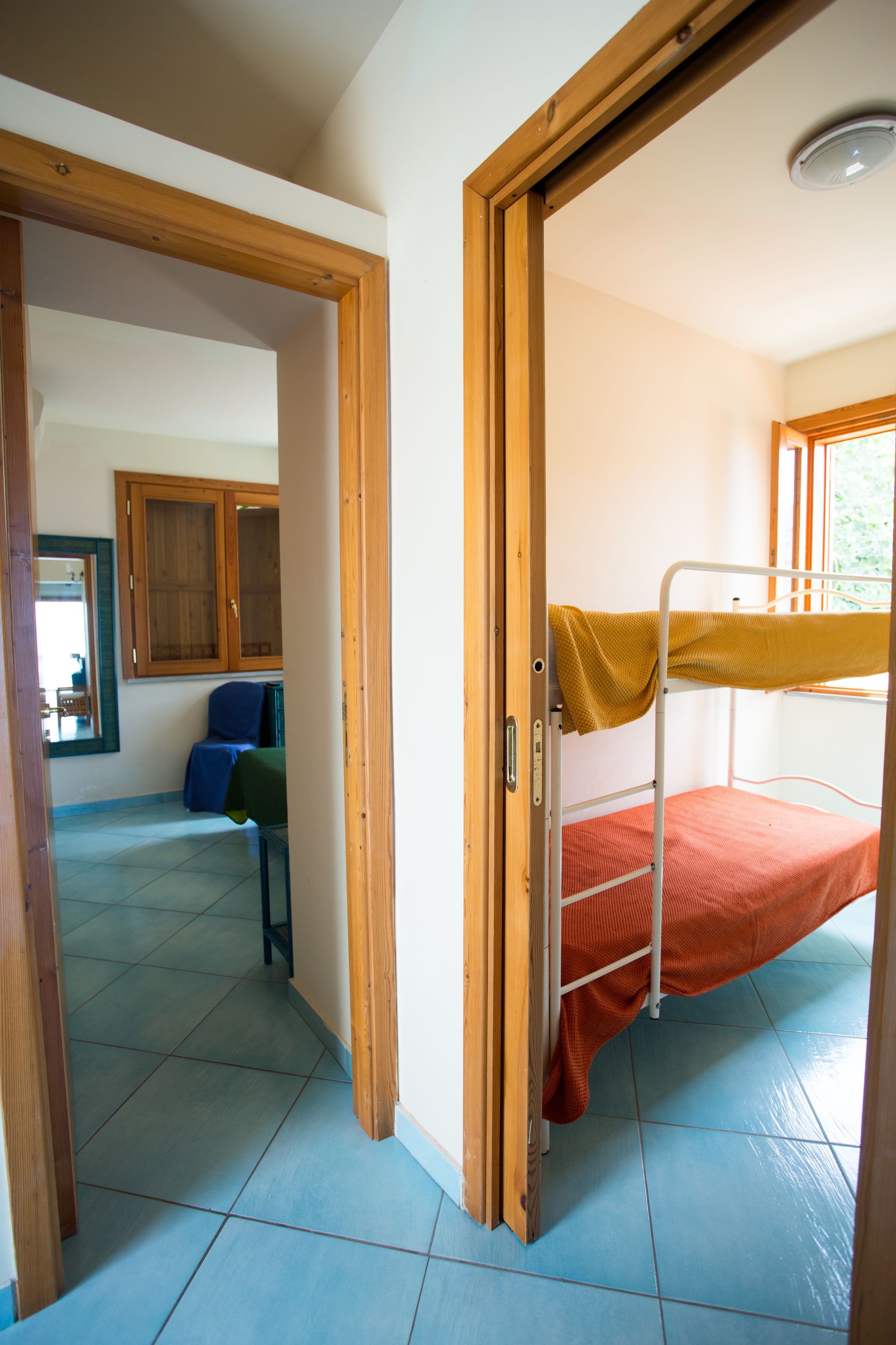 Een kamer met een stapelbed, een houten deur, een stoel en een raam.