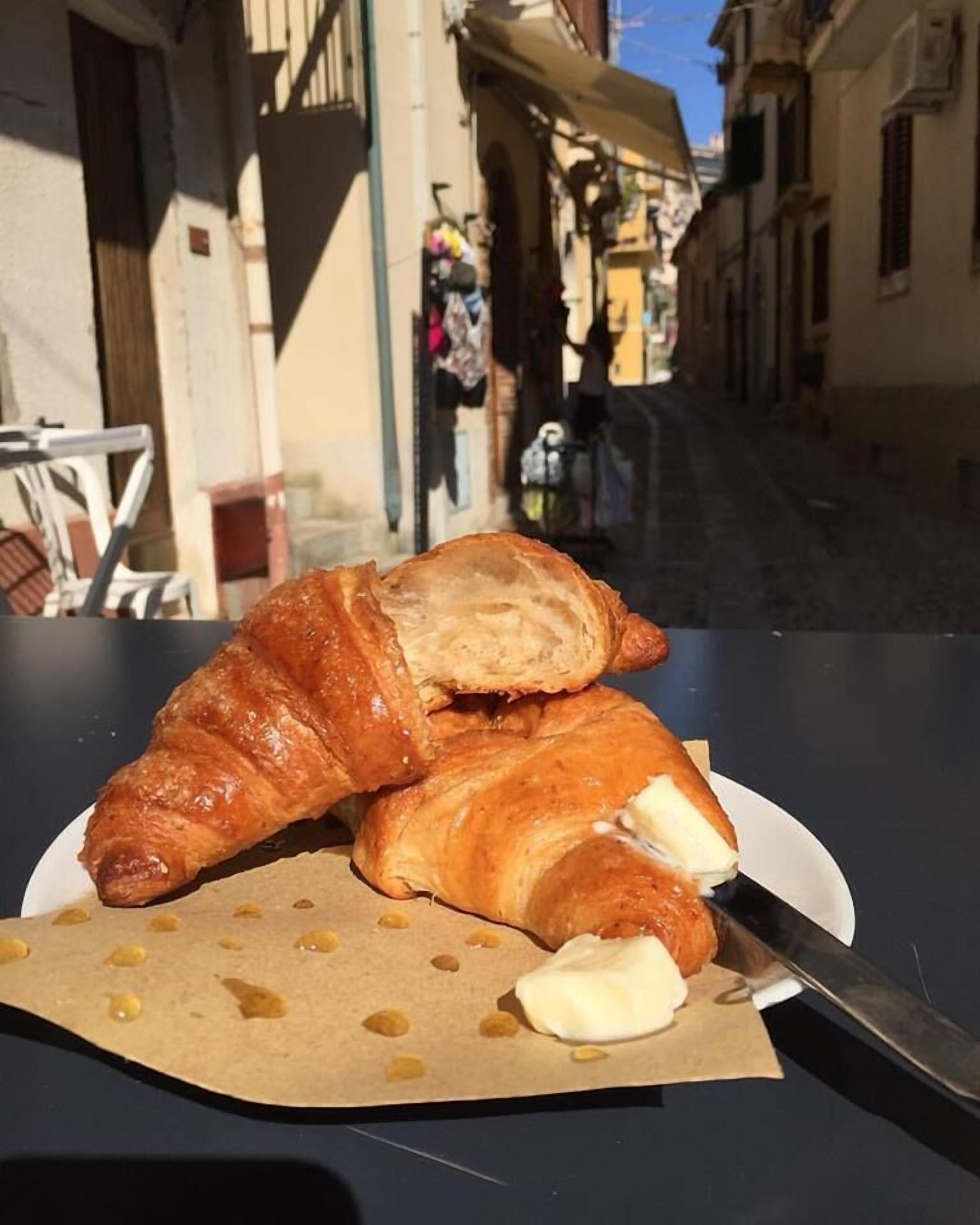 Un croissant en un plato con un cuchillo, sobre una mesa en un espacio al aire libre.