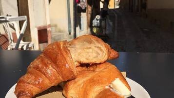 Un croissant en un plato con un cuchillo, sobre una mesa en un espacio al aire libre.