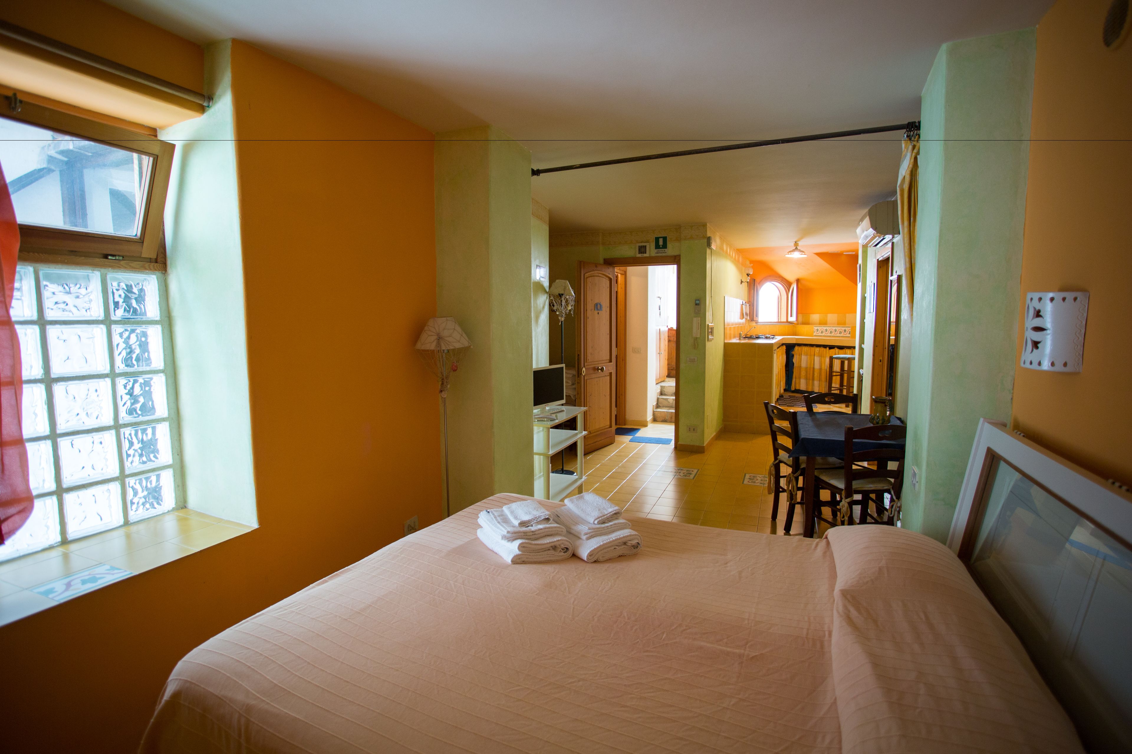 Quarto de hotel com cama, escrivaninha e cadeira. Há uma janela com cortinas e vista para o exterior.