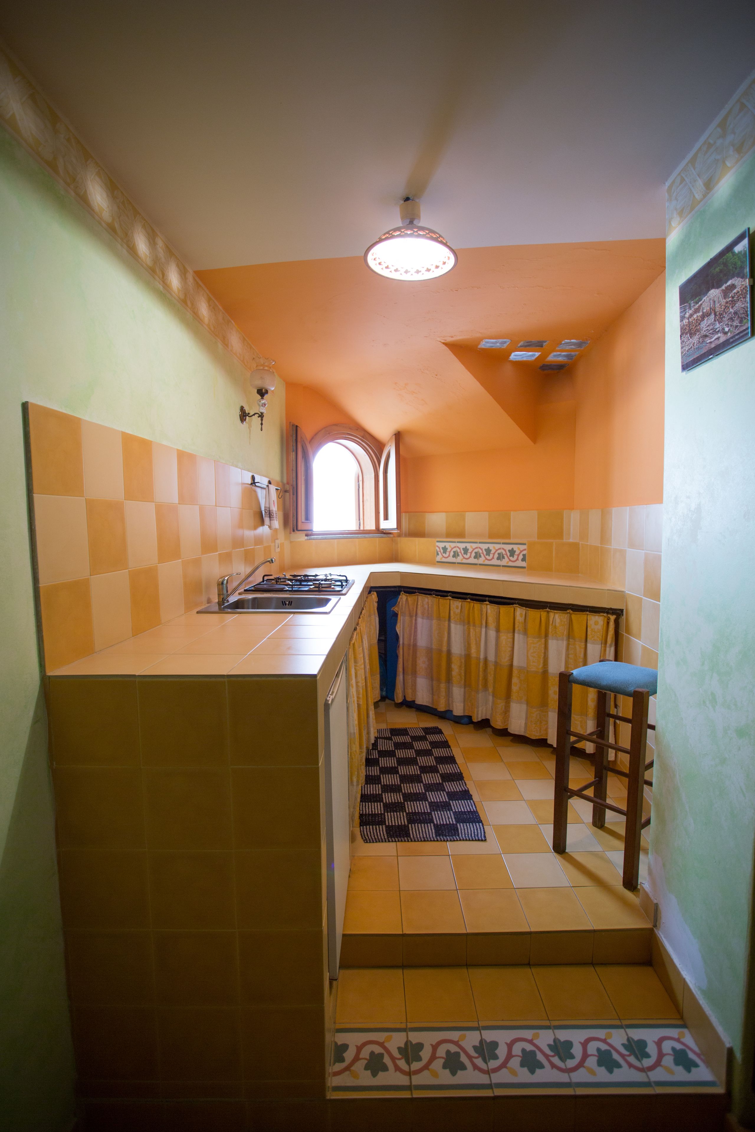 Cocina compacta con estufa a gas empotrada, un lavamanos y una ventana con cortina.