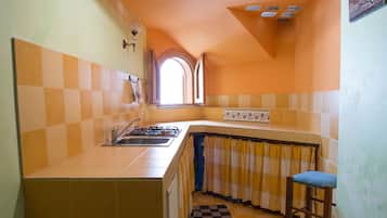 Cocina compacta con estufa a gas empotrada, un lavamanos y una ventana con cortina.