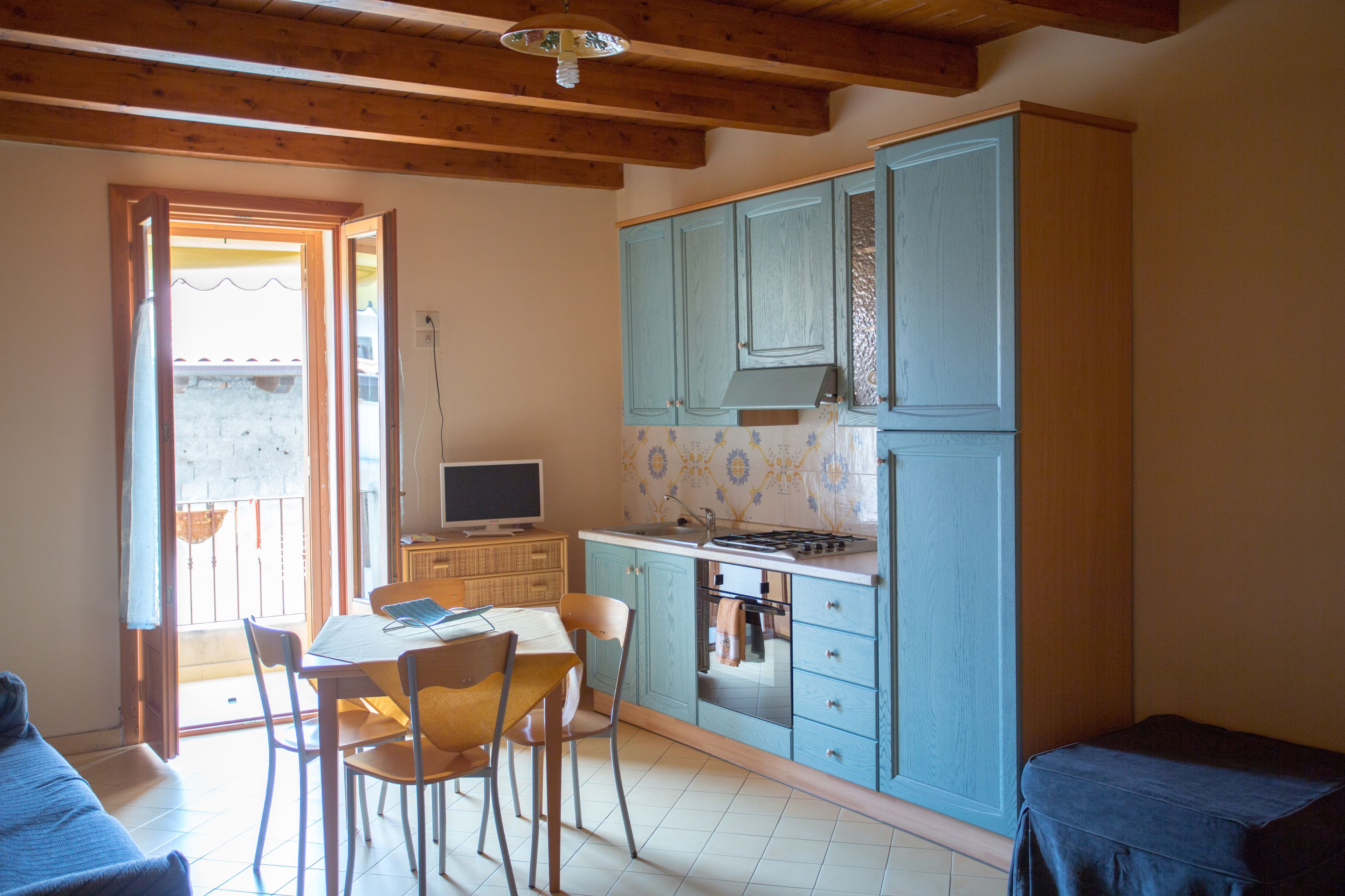Una cucina compatta con mobili blu, un tavolo da pranzo con sedie e un piccolo televisore.