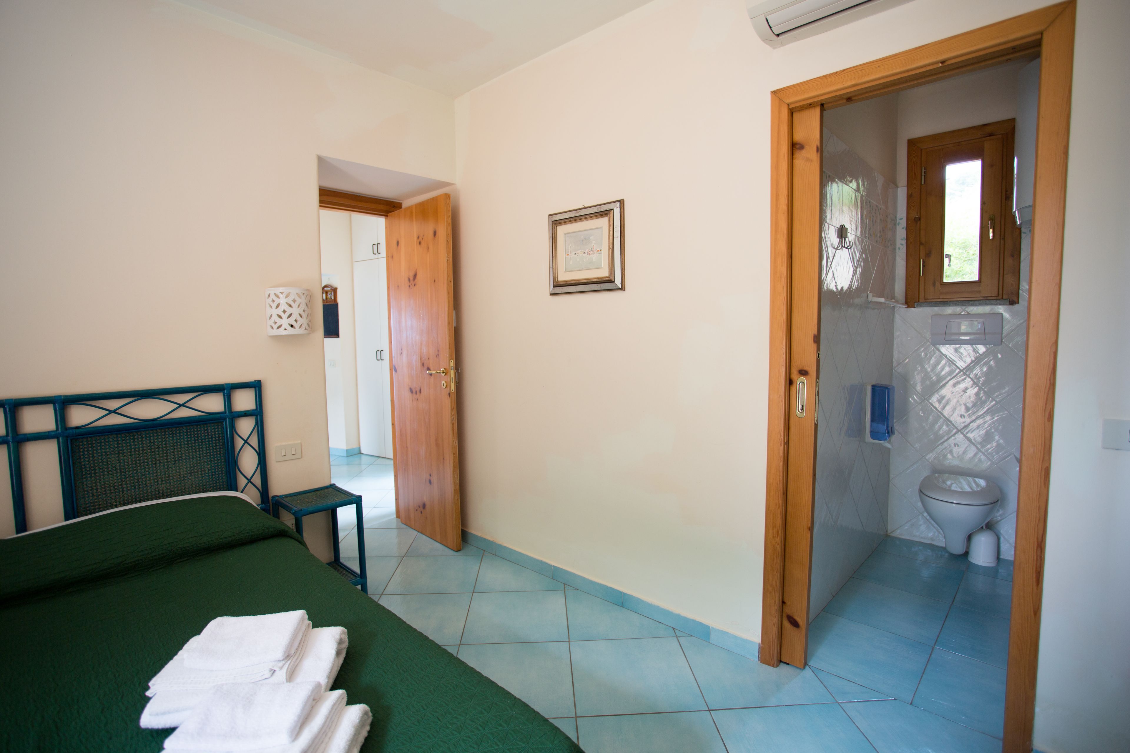 A bedroom with a bed, a bedside table, and a bathroom visible through an open door.