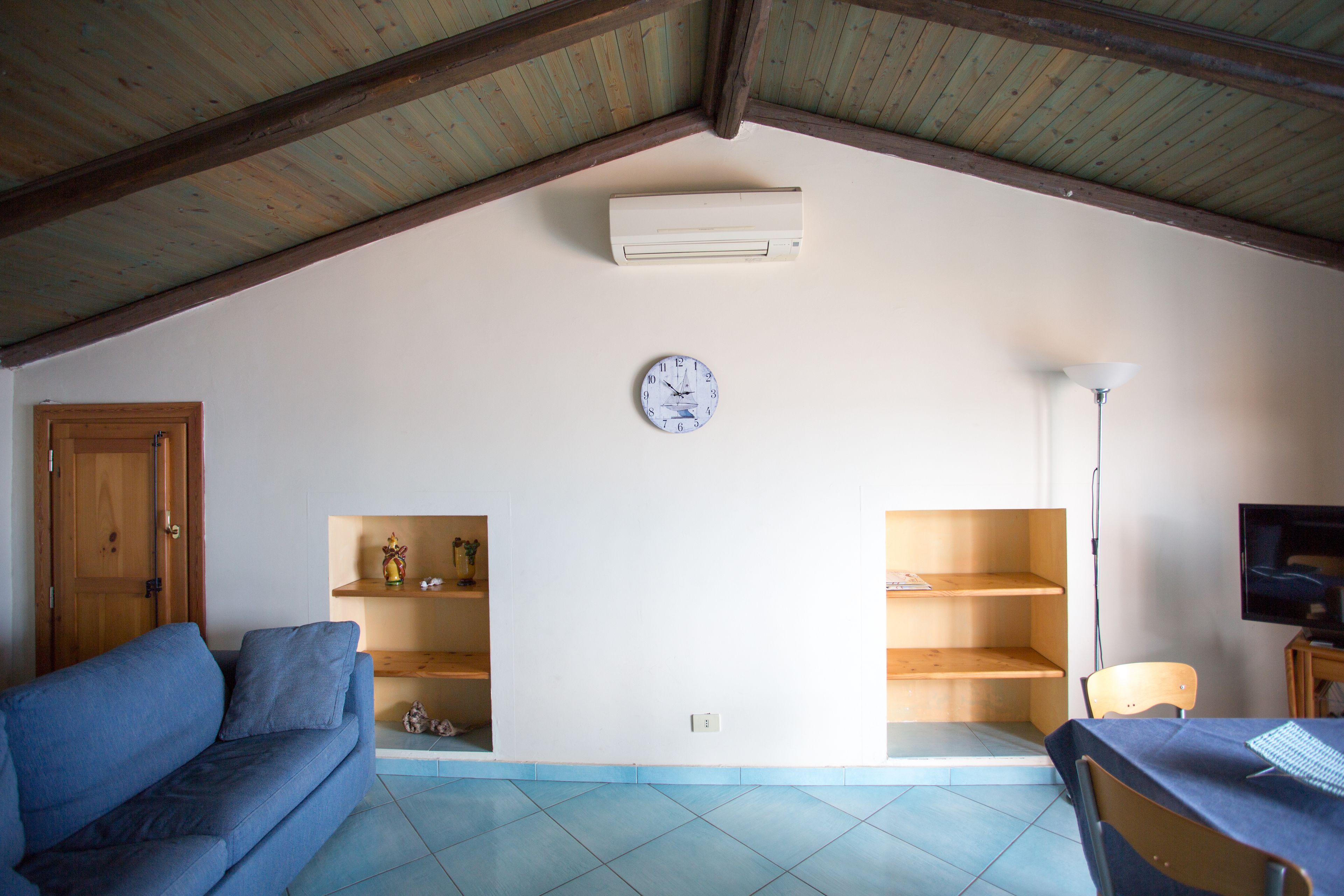 A living room with a blue sofa, wooden shelves, a clock, and a television.
