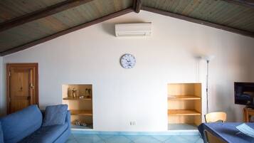A living room with a blue sofa, wooden shelves, a clock, and a television.