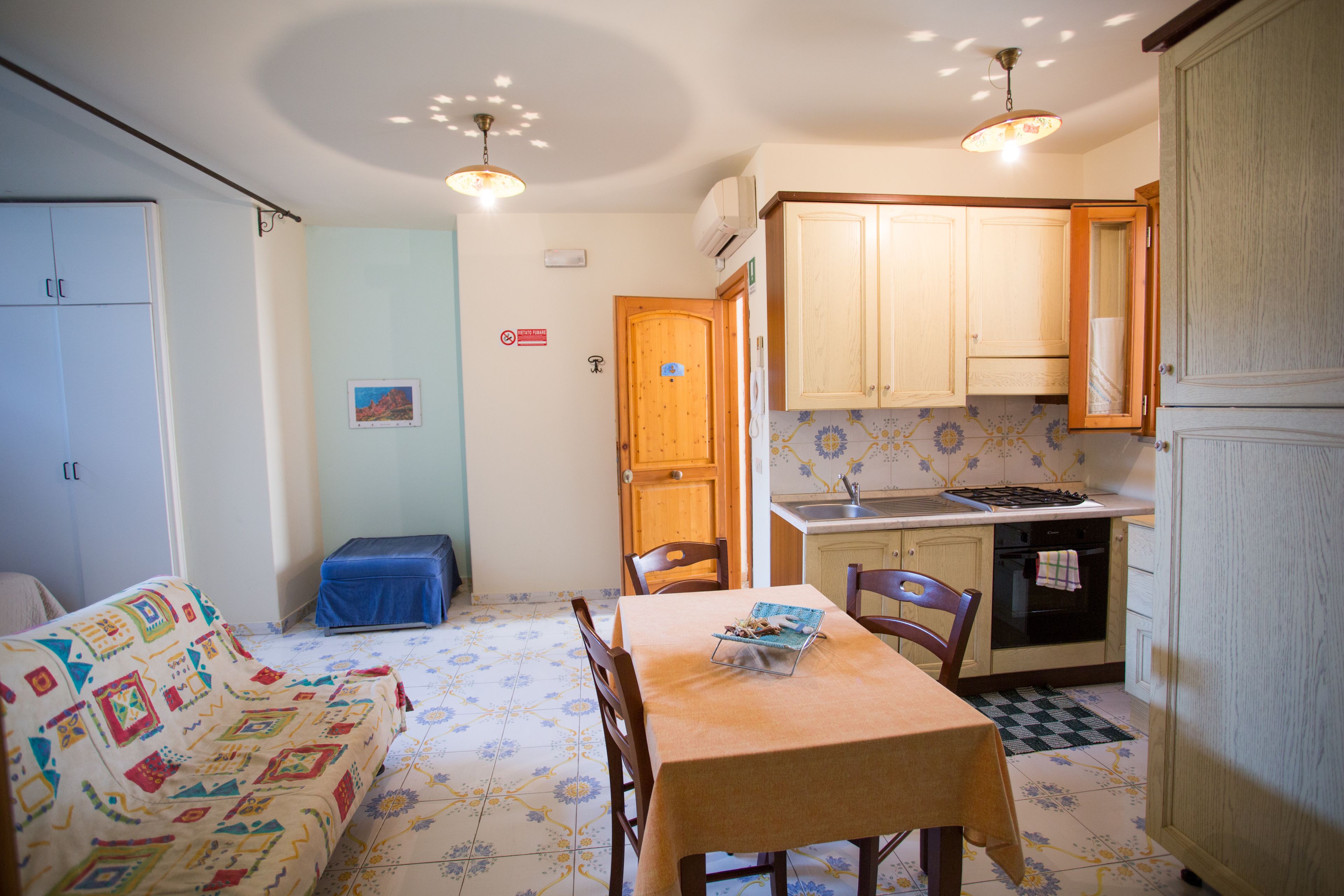 A compact kitchen with wooden cabinets, a dining table, and a blue-covered bench.