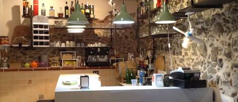 A bar area with shelves stocked with bottles, a counter with a menu, and hanging green pendant lights.