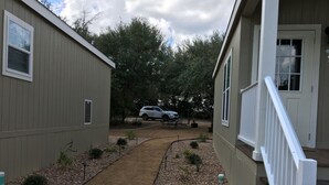 Ein Weg führt zu einem Haus mit weißem Geländer, im Hintergrund ist ein Fahrzeug geparkt.