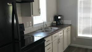 Eine Küche mit einem schwarzen Whirlpool-Kühlschrank, einer doppelten Spüle, weißen Schränken und einer Kaffeemaschine.