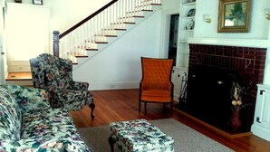 A living room with a floral sofa, an orange armchair, a wooden coffee table, a fireplace, and a staircase.