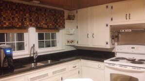 A kitchen with white cabinets, a black countertop, a stainless steel sink, and a white stove.