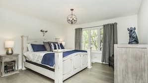 Un dormitorio con cama, mesitas de noche, un candelabro, una ventana con cortinas y una estatua.
