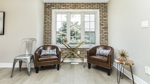 Una habitación con dos sillones de cuero, una silla de metal y una mesita con un objeto decorativo. Se ve una ventana con vistas a árboles.