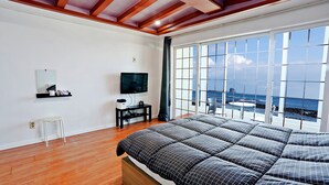Une chambre à coucher avec un grand lit, une télévision, un petit tabouret et une fenêtre donnant sur l’océan.