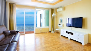 Un salon avec un canapé, un téléviseur et une vue sur la mer, visible à travers une grande fenêtre.