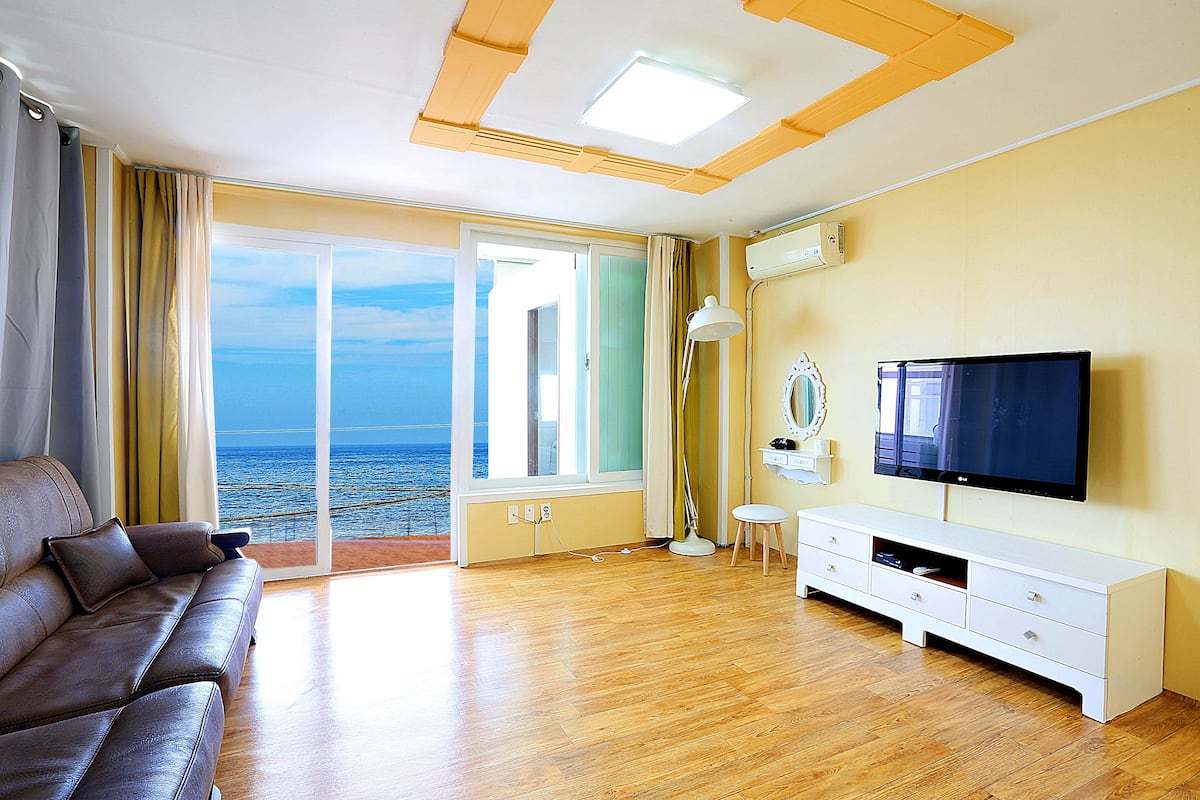 Un salon avec un canapé, un téléviseur et une vue sur la mer, visible à travers une grande fenêtre.