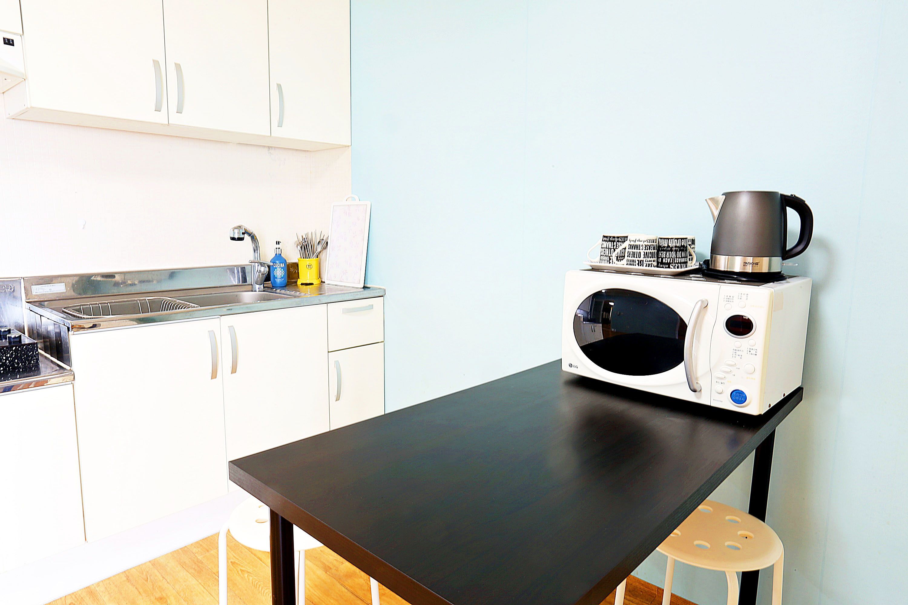 A kitchen with white cabinets, a black countertop, a microwave, and a kettle.