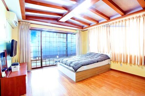 A bedroom with a large bed, wooden flooring, a TV, and a window with curtains.