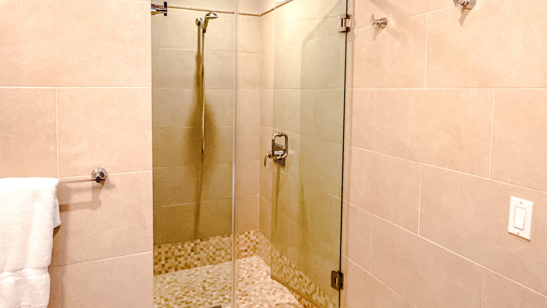 Une douche avec des portes en verre, un porte-serviettes et un carrelage décoré.