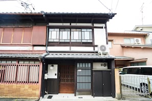 A traditional Japanese house with a wooden front door, sliding glass windows, and a small porch area.
