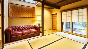 Una habitación tradicional japonesa con suelo de tatami, un sofá de cuero, un puertas correderas y un tapiz decorativo.