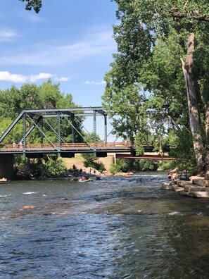 Un puente metálico sobre un río con gente en una balsa.