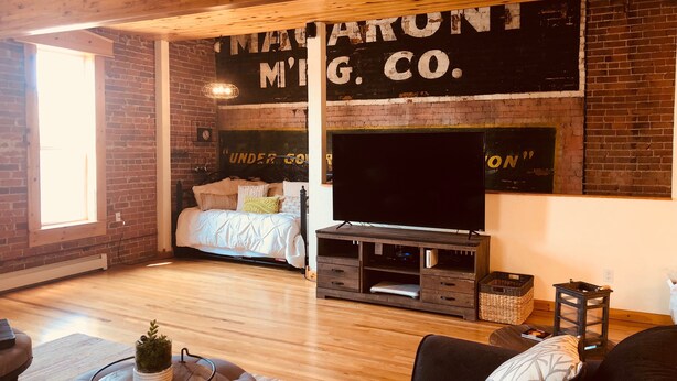 A cozy living room with a brick wall, a bed, a TV, and a fireplace. - 2 Bedroom, 1 Bath Townhouse in Historic Downtown Florence! (Florence)