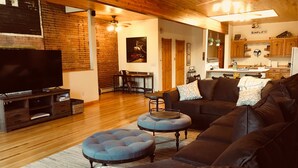 A modern living room with a large flat-screen TV, dark leather sofas, and a blue ottoman. - 2 Bedroom, 1 Bath Townhouse in Historic Downtown Florence! (Florence)