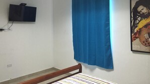 Un dormitorio con una cama individual, una cortina azul, un televisor montado y un cartel en la pared.