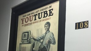 Póster enmarco que anuncia YouTube, mostrando a un hombre sentado en un escritorio con una computadora.