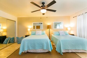 A hotel room with two beds, a ceiling fan, bedside lamps, a mirror, and a window with curtains. - 4 bedroom, 2.5 bath, Sleeps 9 in beds (Haleiwa)