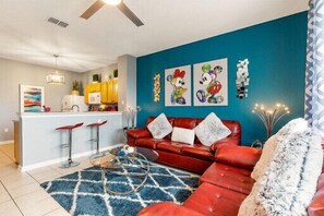 A living room with a red sofa, a blue rug, and a kitchen area with yellow cabinets.