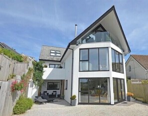 A modern two-story house with a flat roof, large windows, and a patio area with outdoor furniture. - Luxury ground floor Apartment Sleeps 5 (mevagissey)