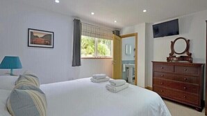 Une chambre d’hôtel avec un lit, une commode, une t élévision et une fenêtre avec des rideaux.